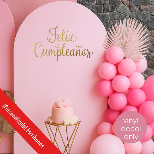 Pink birthday backdrop with “Feliz Cumpleaños” gold vinyl decal, Spanish party decoration with balloons and cake.