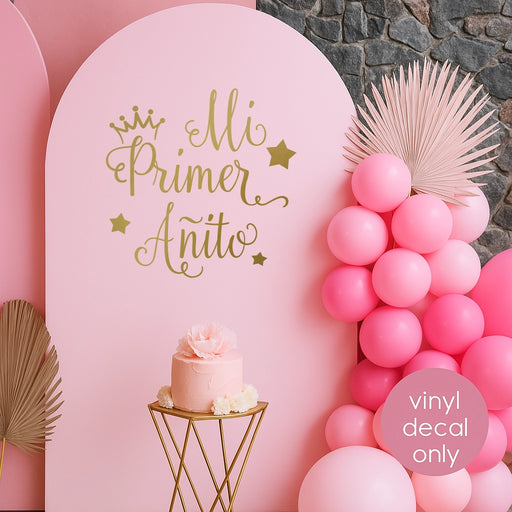 Pink backdrop with gold “Mi Primer Añito” vinyl decal featuring crown and stars, designed for Spanish first birthday celebration decoration.
