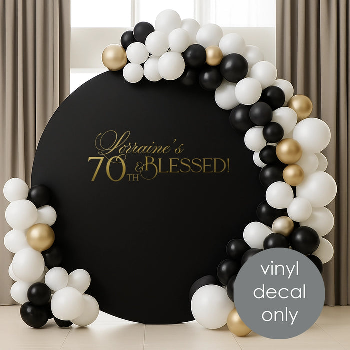 Elegant gold vinyl decal “Lorraine’s 70th & Blessed” on black round backdrop with white and gold balloons for milestone birthday decoration