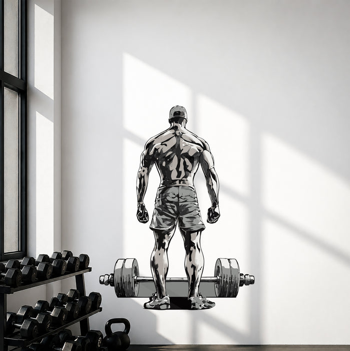 Bodybuilder standing before a barbell wall decal in a gym with dumbbells